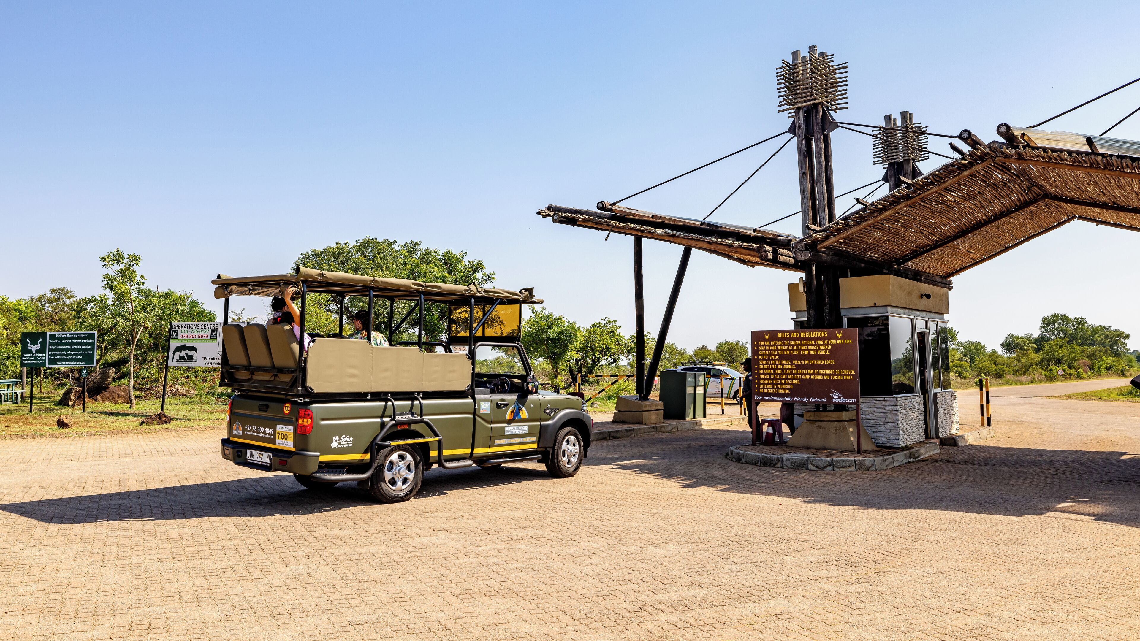 A safari vehicle at a gate with a sign detailing rules and regulations.