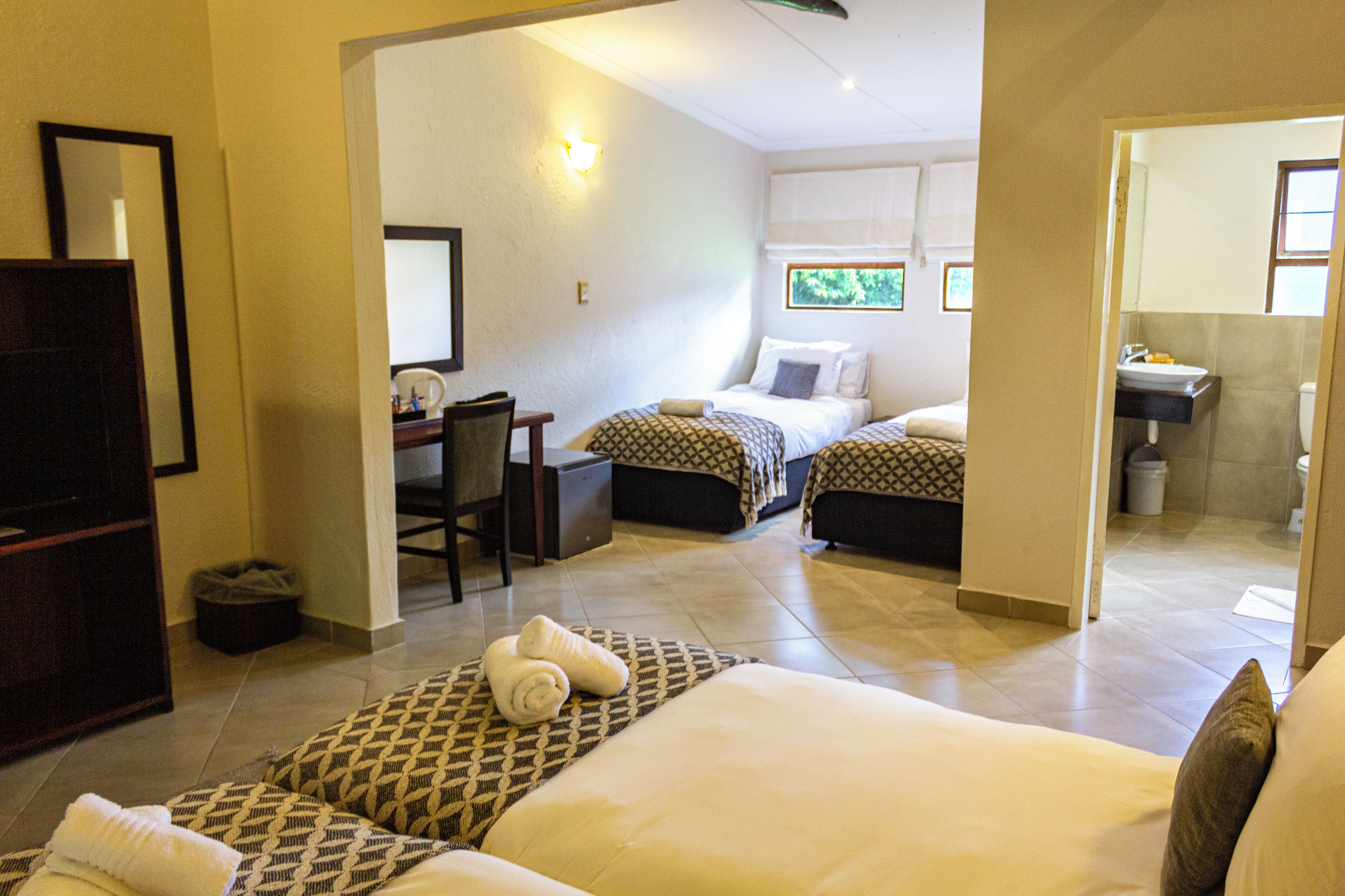 A hotel room with a large bed, two smaller beds, a desk, and a bathroom.
