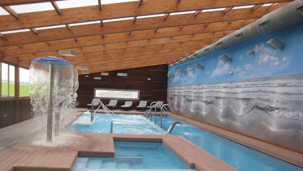 Ein Innenpool mit Wasserspiel, Liegestühlen und einem Meeresmural.