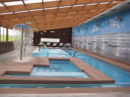 An indoor swimming pool with a water feature, lounge chairs, and a mural of the ocean.