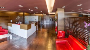 Eine moderne Lobby mit roten Ledersesseln, einem Empfangstresen und einer Glastrennwand.