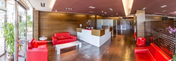 Un moderno vestíbulo con asientos de cuero rojo, un mostrador de recepción y una partición de vidrio.