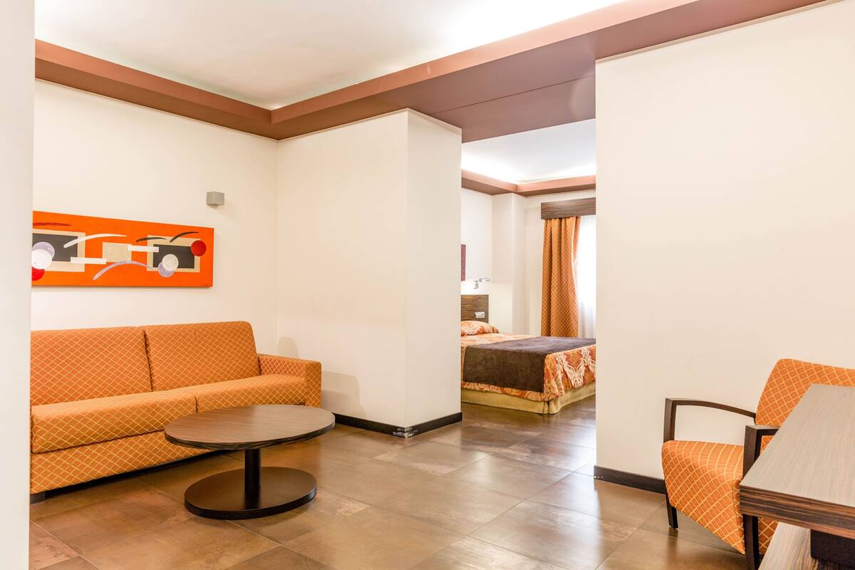 A hotel room with a sofa, a round table, and a bed with an orange bedspread.