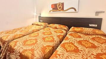 Habitación con tres camas, cada una con ropa de cama estampada, cabeceros oscuros y una obra de arte colgada en la pared.