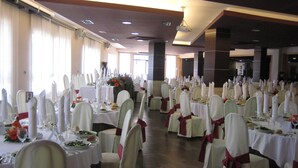 Ein Festsaal mit Tischen, gedeckt für eine festliche Veranstaltung, mit weißen Tischdecken, ordentlich gestellten Stühlen und floralen Mittelpunkten.