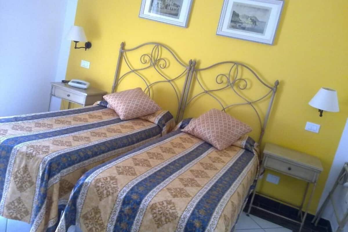 A room with two beds, a nightstand, a lamp, and two framed pictures on the wall.