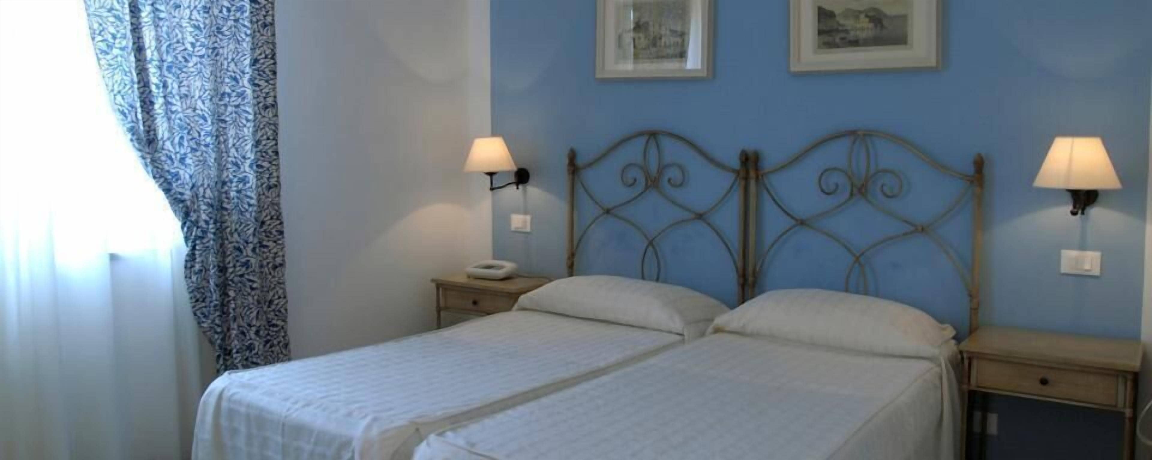 A bedroom with a double bed, two bedside tables, and two wall-mounted lamps.