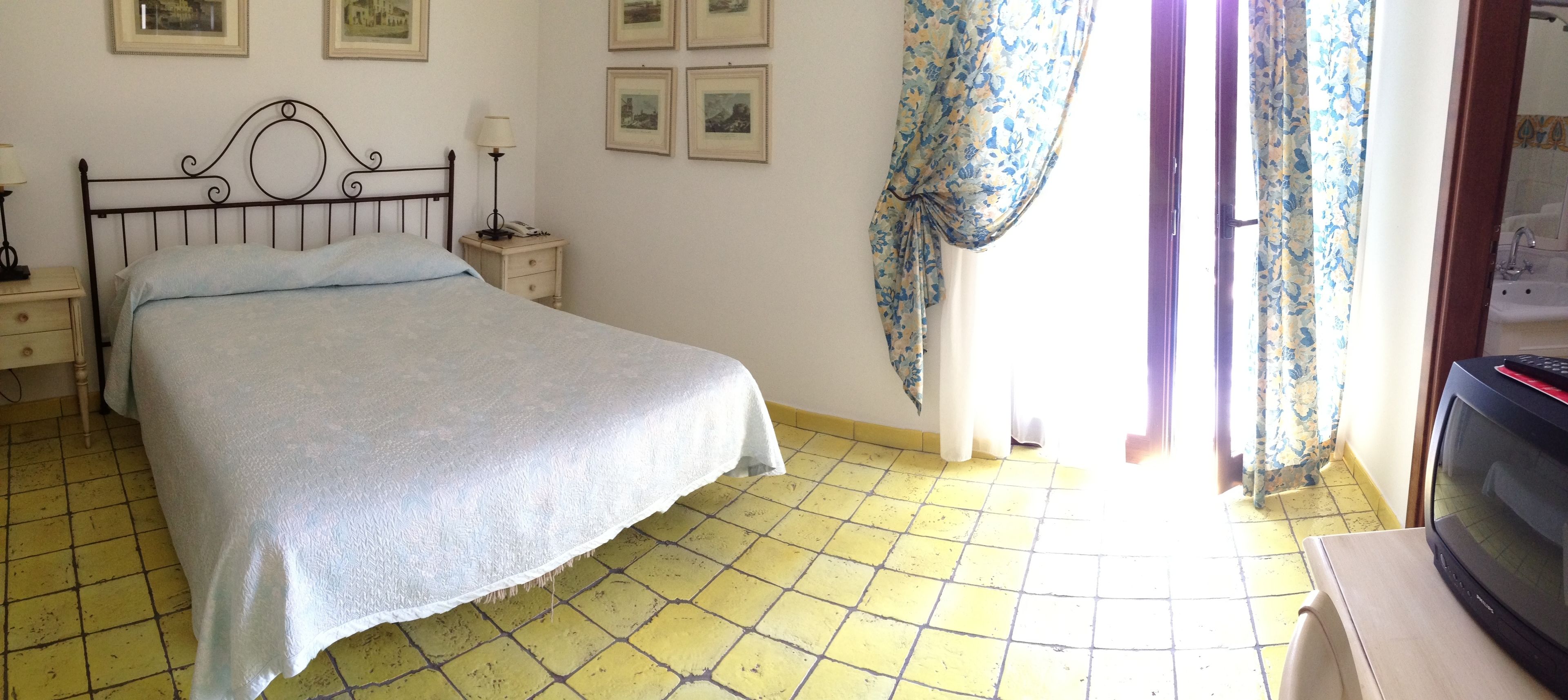 A bedroom with a bed, a nightstand, a lamp, a telephone, and a television.