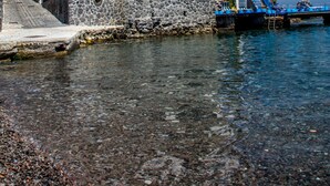 A white building with blue balconies, a stone base, and a clear blue sky. - Rocce Azzurre (Lipari)