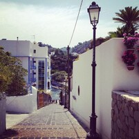 Una estrecha calle adoquinada con un farol y un edificio blanco con detalles azules.