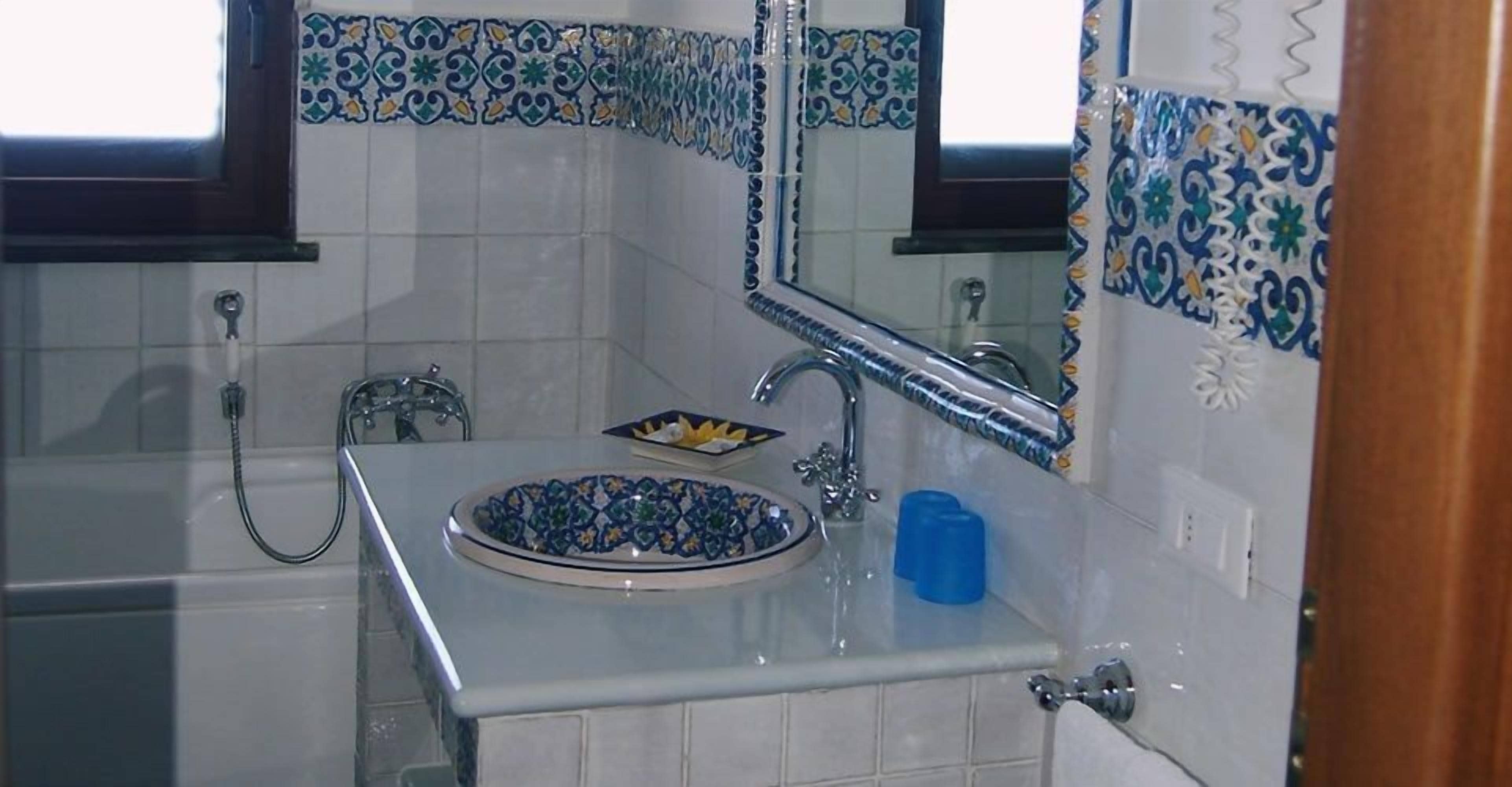 Ein Badezimmer mit Waschbecken, Fliesen in Blau und Grün mit Muster, Spiegel und Badewanne.