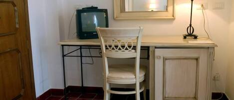 Una habitación pequeña con una puerta de madera, una silla blanca, un televisor sobre una mesa y un espejo en la pared.