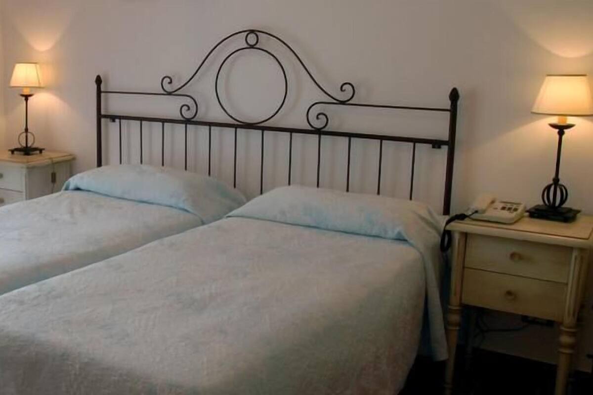 A double bed with a metal headboard, two bedside tables with lamps, and a small bedside drawer.