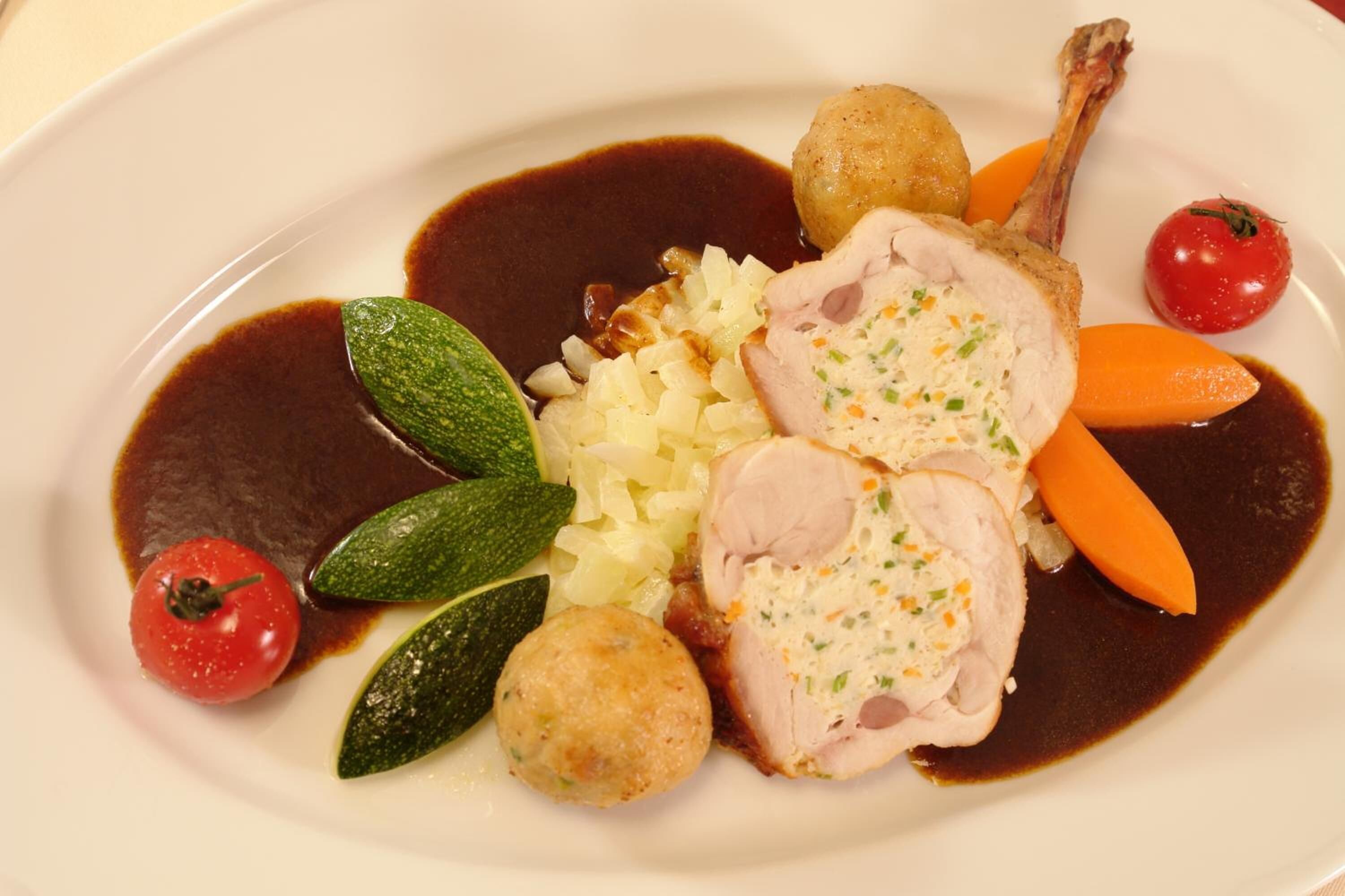A plate of food with sliced meat, vegetables, and a sauce.