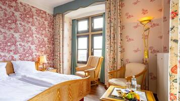 Ein Hotelzimmer mit einem Bett, zwei Stühlen, einem Tisch mit Obst und einem Vorhangfenster.