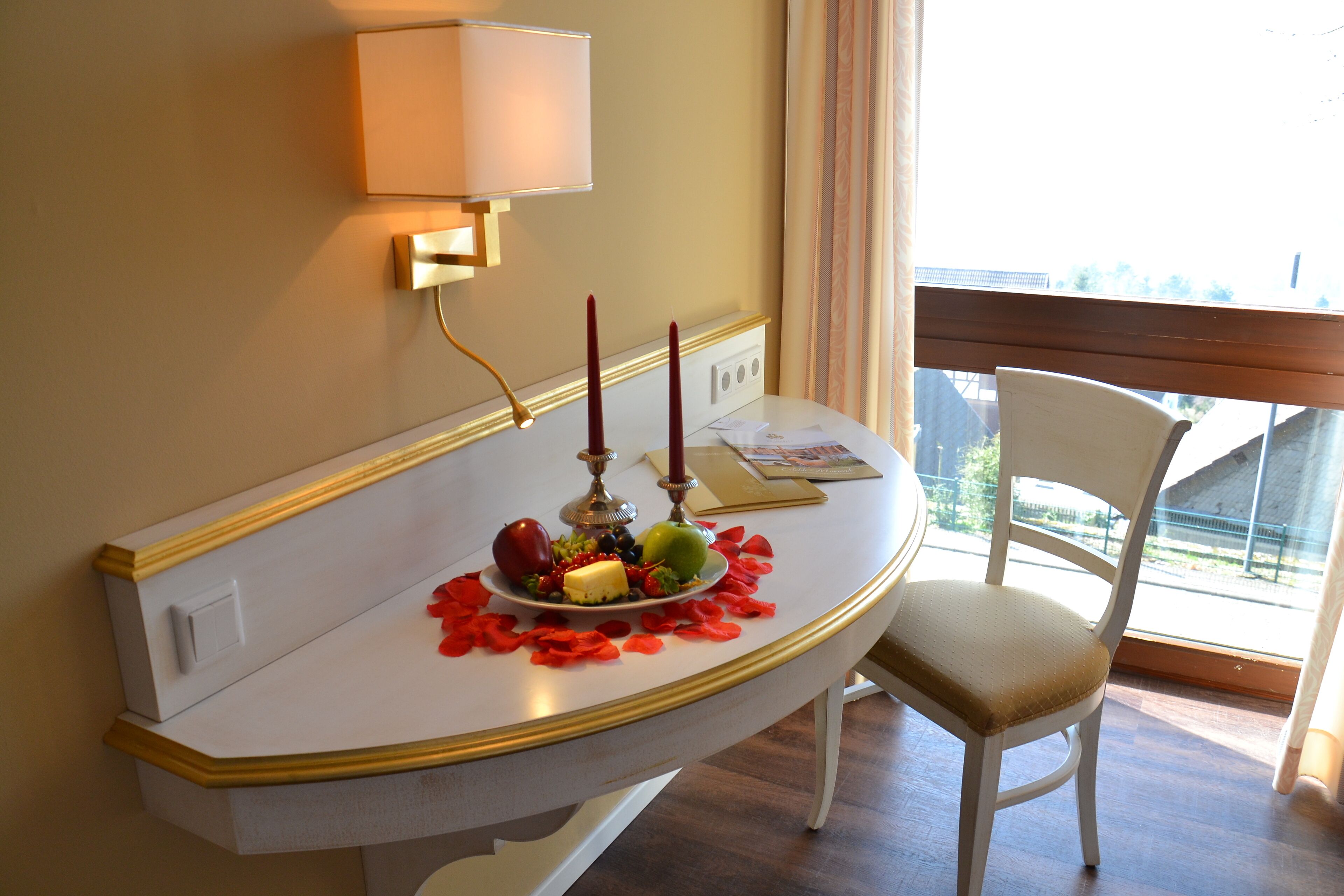 Une table à manger au design blanc et doré, une chaise blanche et une fenêtre donnant sur des immeubles.