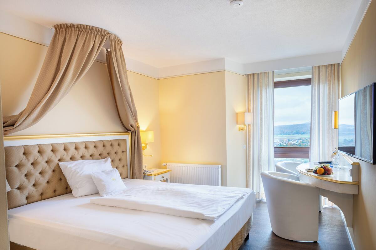 A hotel room with a large bed, a desk with a chair, a window with a view, and a television.