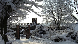 A snow-covered pathway leading to a historic building with a stone archway and a brick bridge.