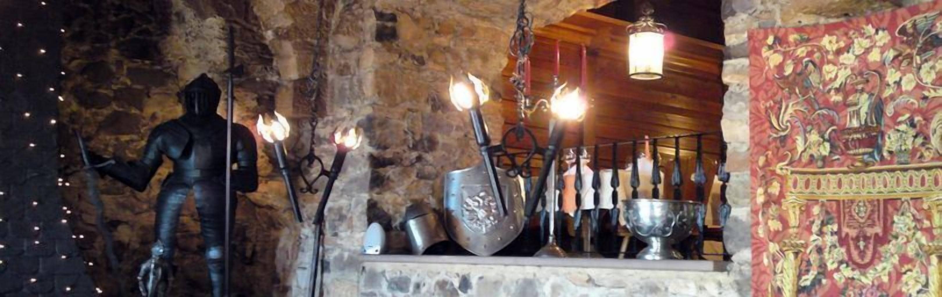 Ett interiört utrymme med stenväggar, en staty av en riddare, metallföremål och en hängande lampa.