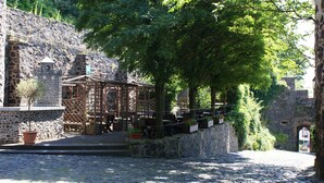 A cobblestone street with a wooden gazebo, stone walls, and lush greenery.