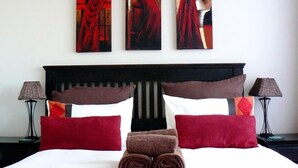 A hotel room with a bed, pillows, a headboard, two nightstands, and three paintings on the wall. - See More Guest House (East London)