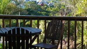 A wooden deck with a table and chairs, overlooking a residential area with houses and lush greenery. - See More Guest House (East London)