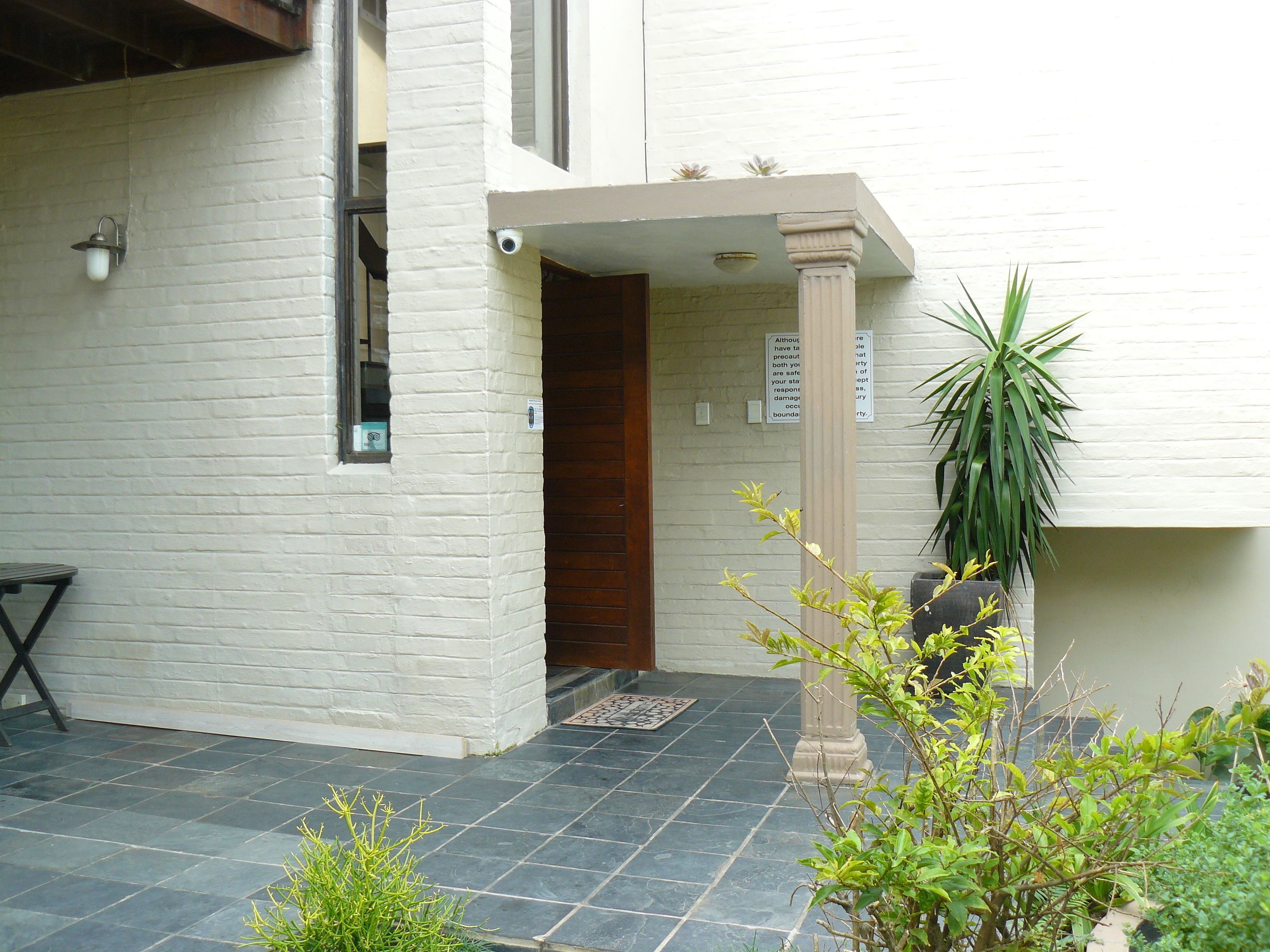 A white building with a wooden door, a potted plant, and a sign on the wall.