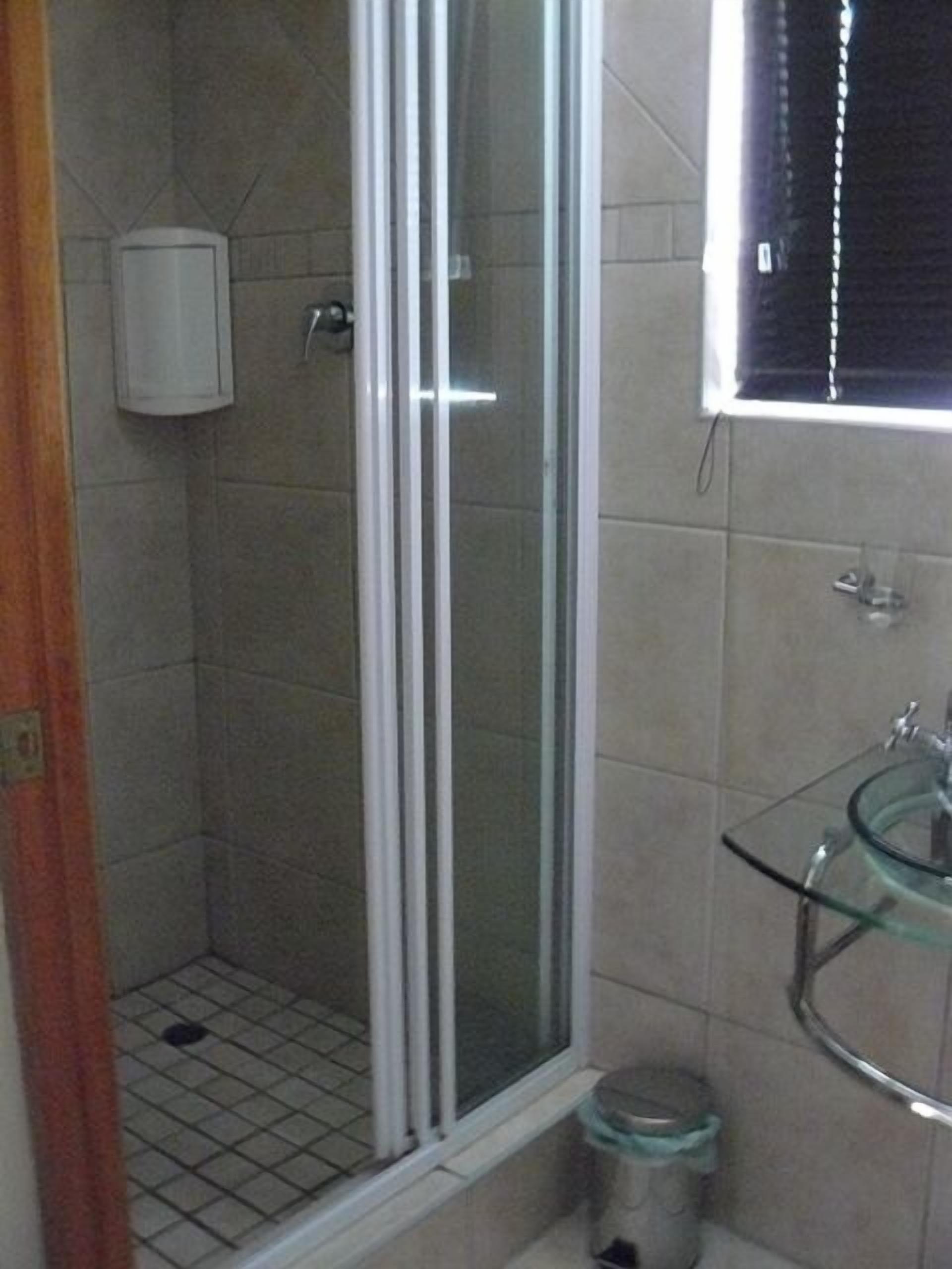 A bathroom with a glass shower enclosure, a glass sink, and a toilet.