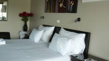 A neatly made bed with white linens, a vase with red flowers, and a painting on the wall.