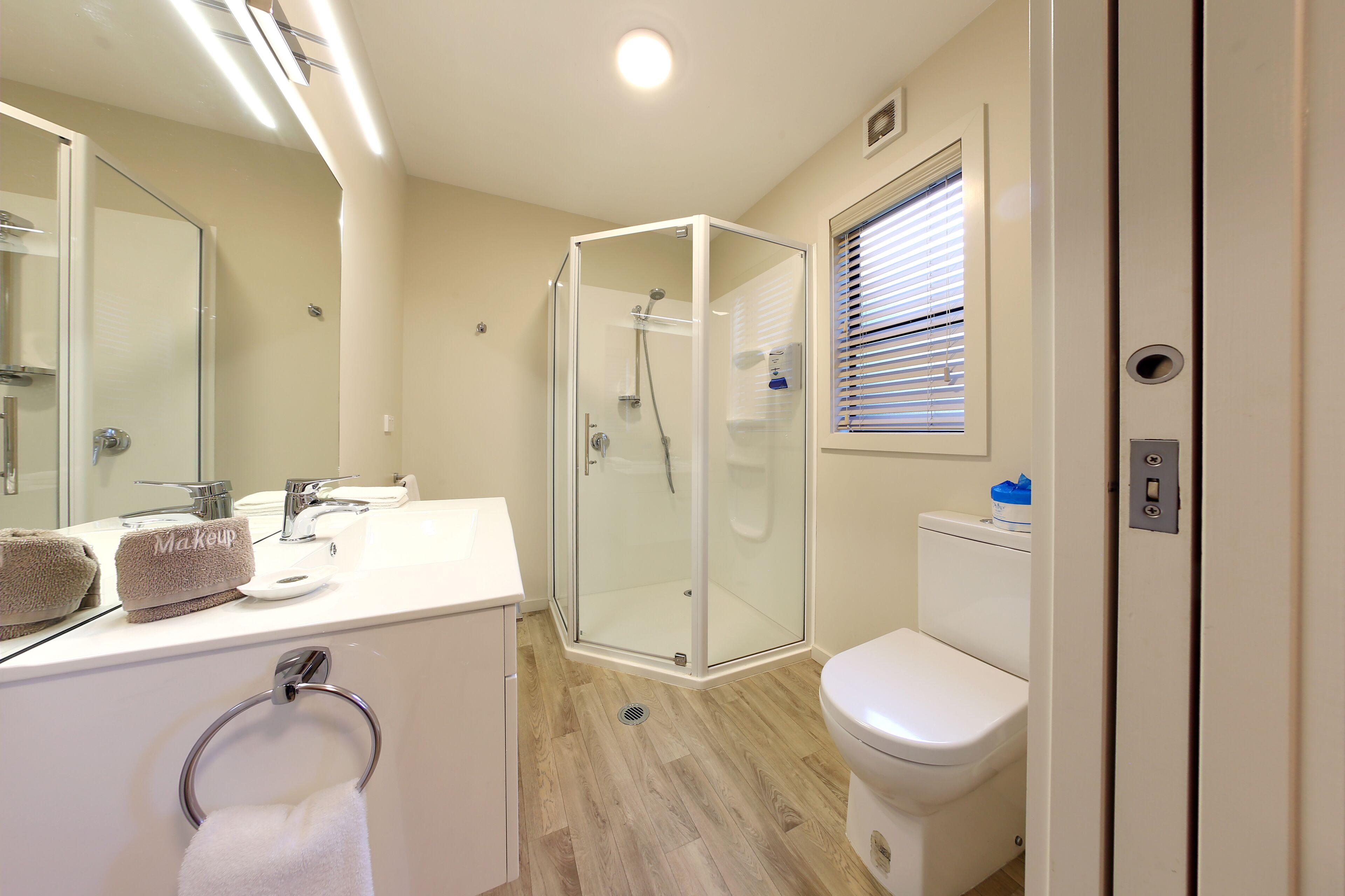 A modern bathroom with a glass-enclosed shower, a white sink with a makeup towel, and a toilet with a window above it.