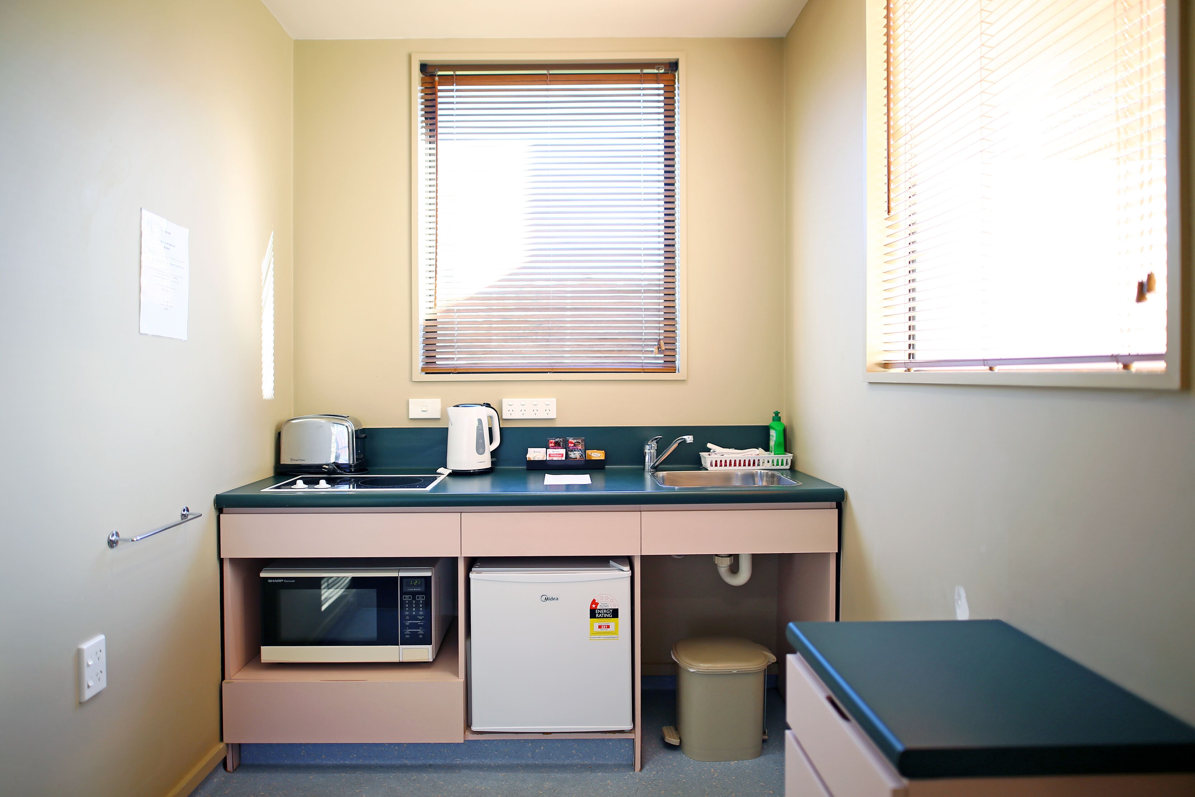 Una kitchenette equipada con microondas, refrigerador, lavamanos y un pequeño cubo de basura.