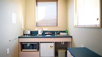 Una kitchenette equipada con microondas, refrigerador, lavamanos y un pequeño cubo de basura.