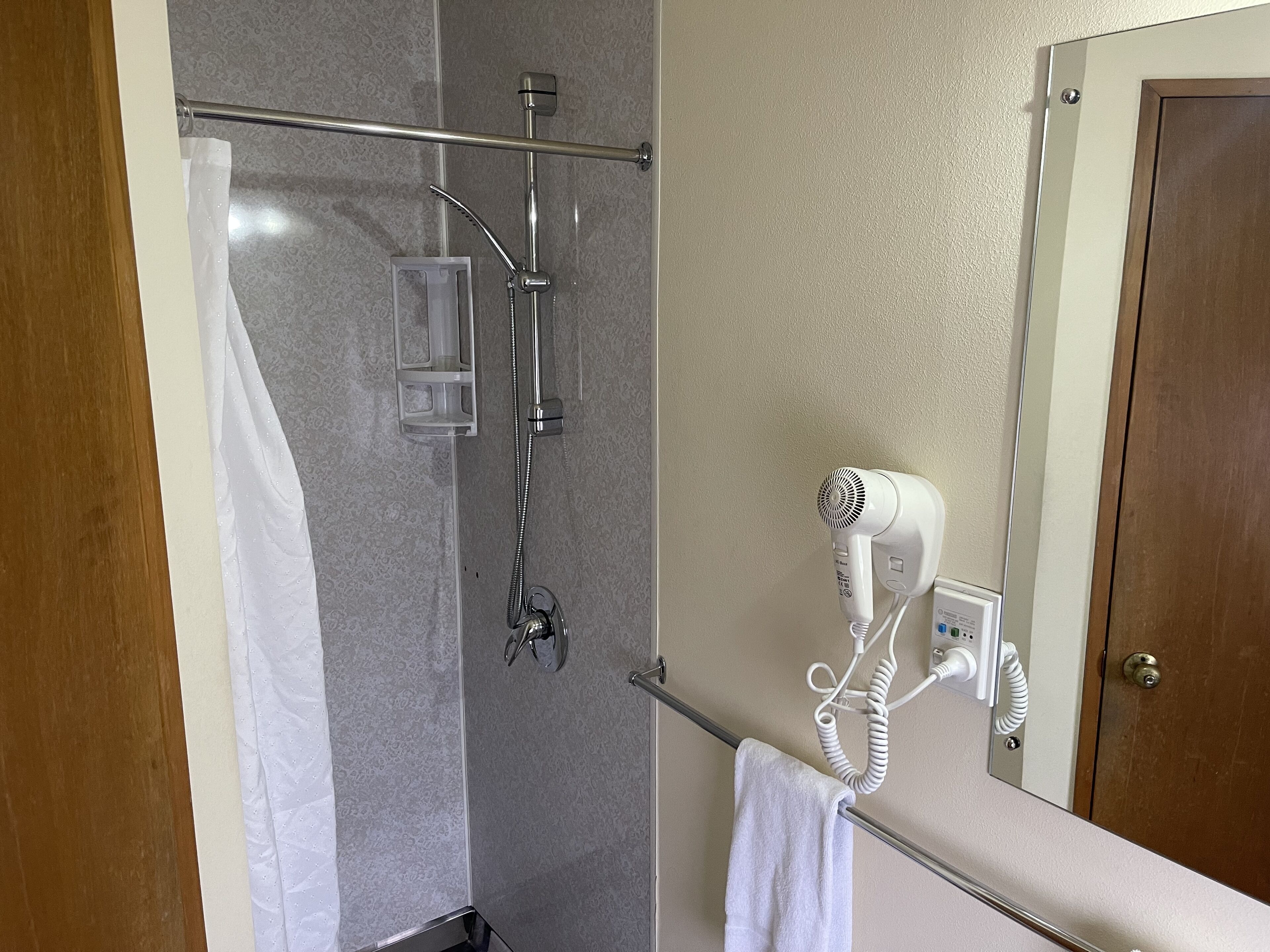 Une salle de bain équipée d’une douche, d’un porte-serviettes et d’un sèche-cheveux fixé au mur.