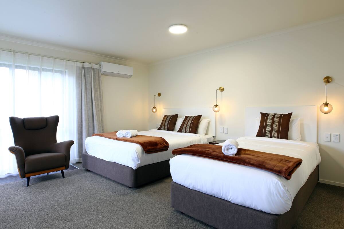 Ein Hotelzimmer mit zwei Betten, einem Sessel und einem Fenster mit Vorhängen.