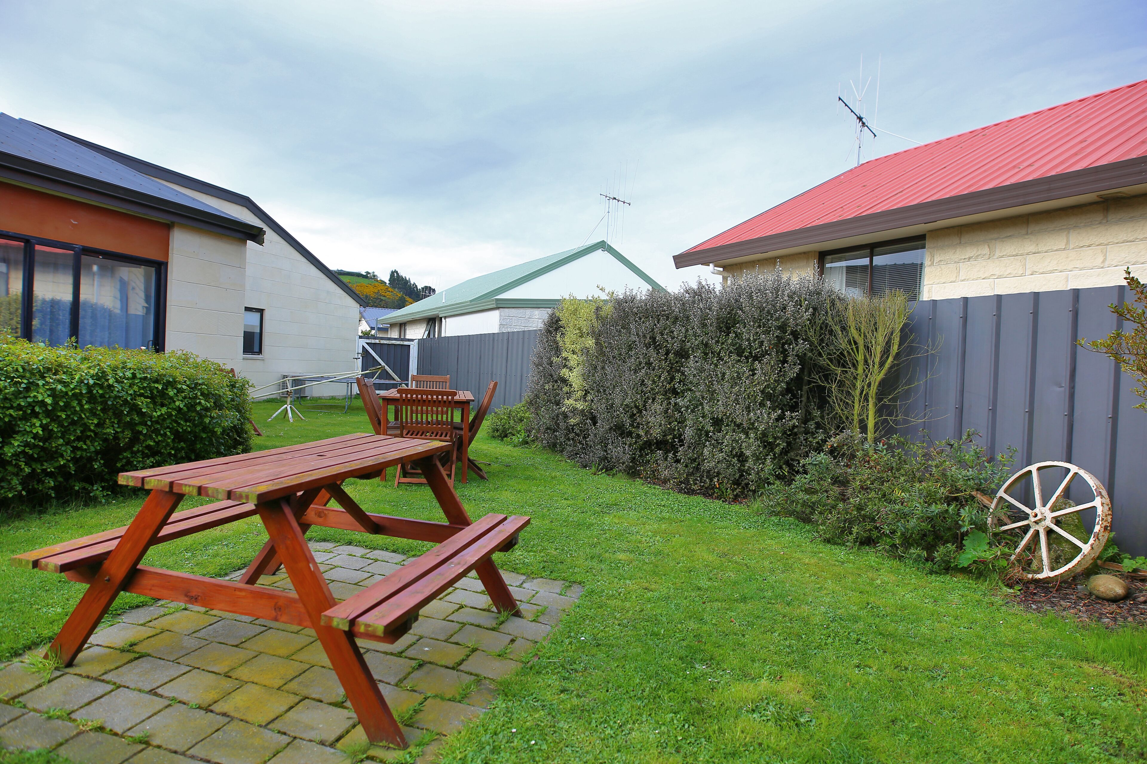 A backyard with a picnic table and chairs, a wooden fence, and a wheelbarrow.