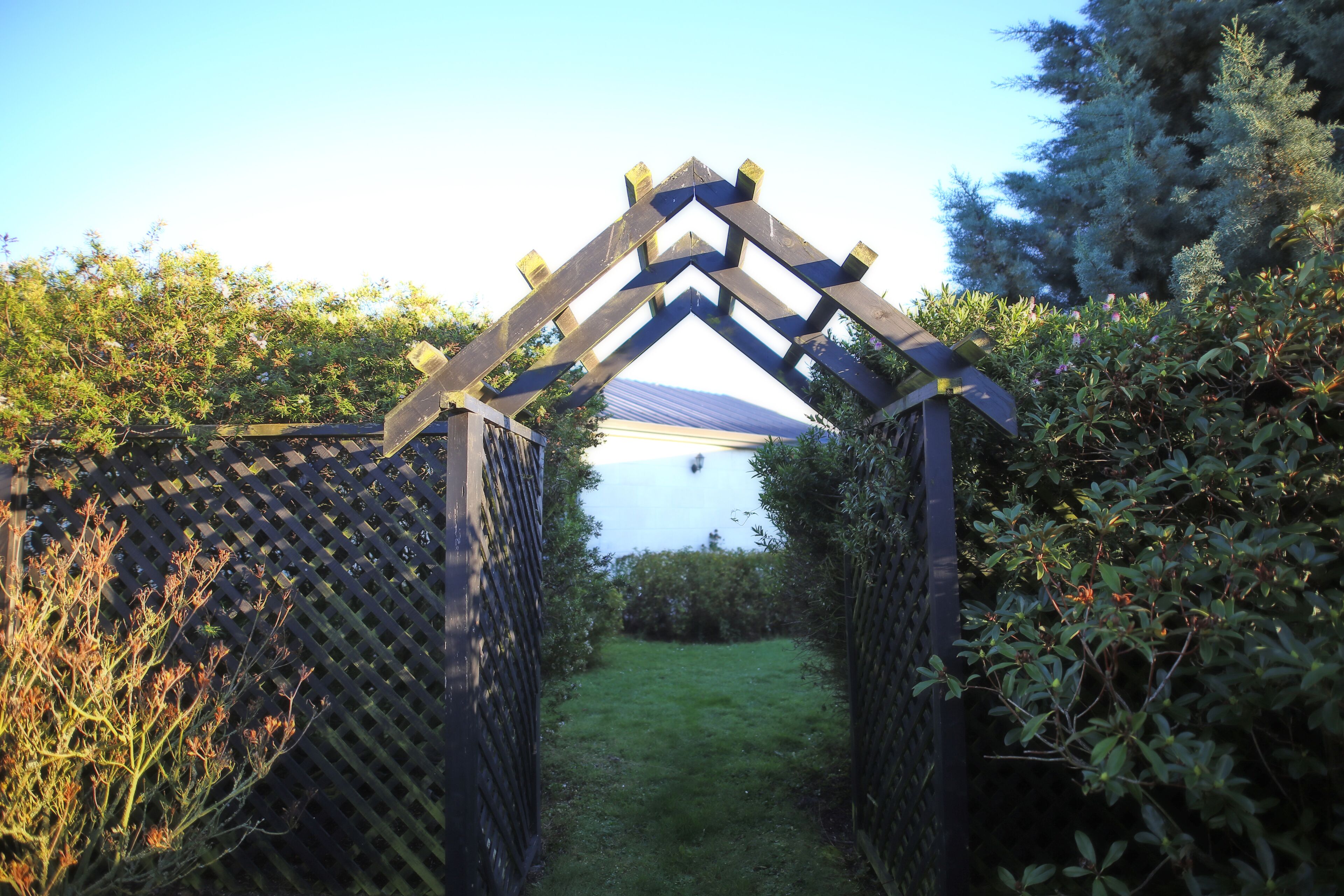 A wooden archway with a lattice on either side, leading to a grassy area.
