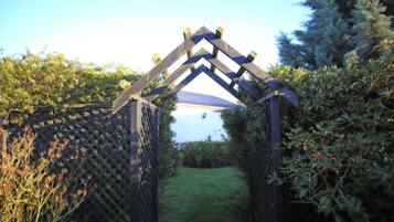 A wooden archway with a lattice on either side, leading to a grassy area.