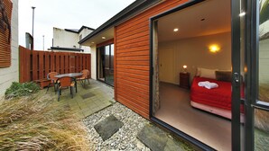 Ein modernes Schlafzimmer mit einem roten Bett, einer Schiebetür und einem kleinen Patio mit Tisch und Stühlen.