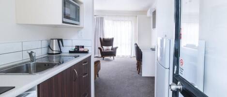 A compact kitchen with a microwave, sink, and coffee maker, leading to a dining area with a chair and a table.