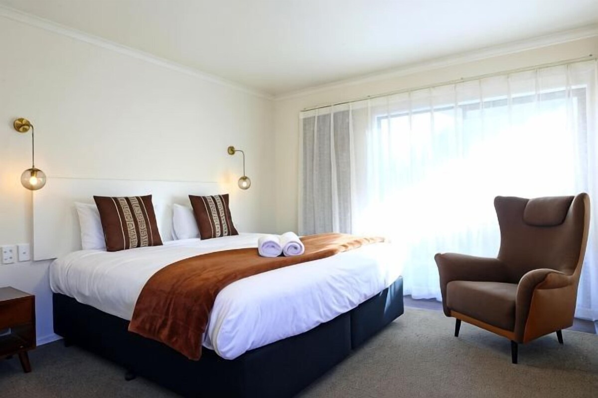 A hotel room with a bed, a chair, and a window with curtains.