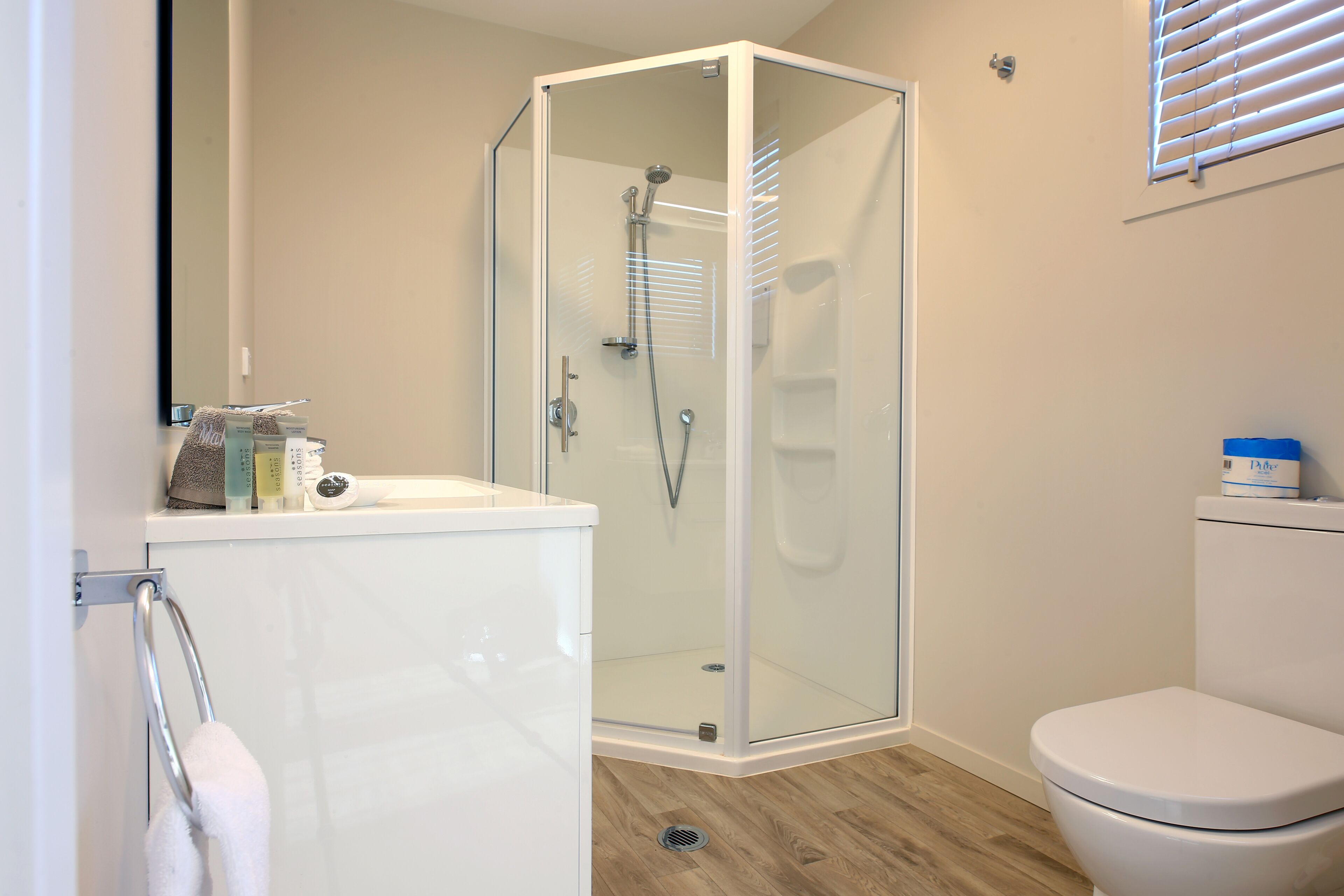 A modern bathroom with a glass-enclosed shower, a white toilet, and a wooden floor.