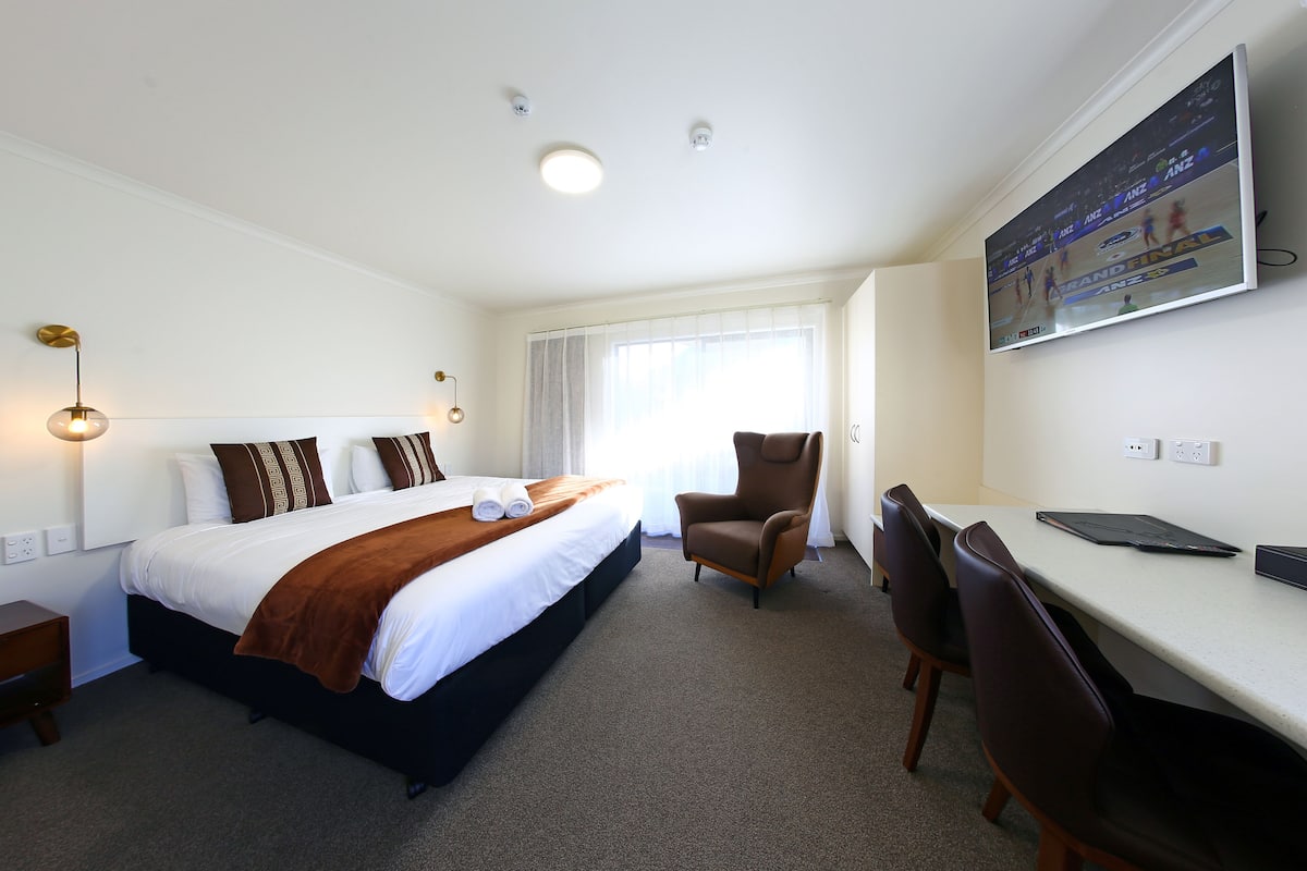 Ein Hotelzimmer mit Bett, Schreibtisch, Stuhl, Fernseher und Fenster.