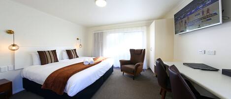 Ein Hotelzimmer mit Bett, Schreibtisch, Stuhl, Fernseher und Fenster.
