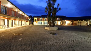 Ein Hotelinnenhof mit gepflastertem Weg, einem Palmenbeet und einem Gebäude mit mehreren Balkonen und Fenstern.