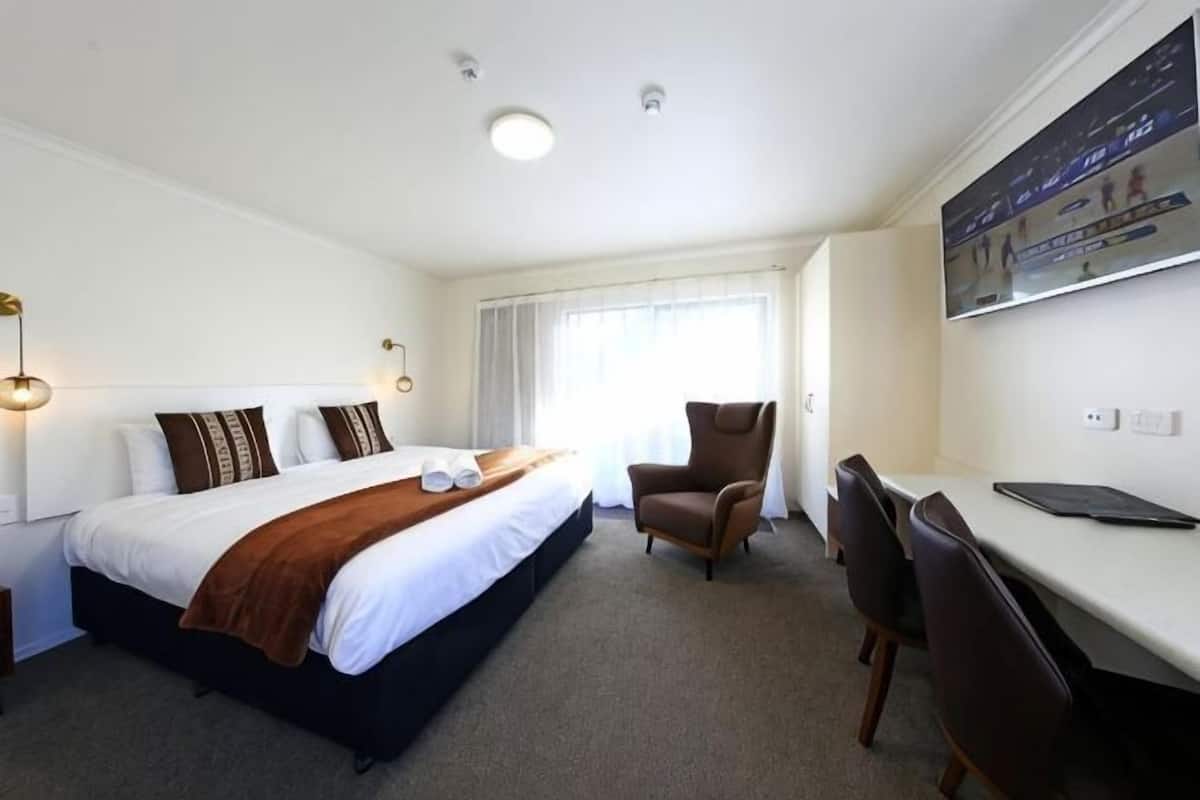 A hotel room with a bed, a desk, a chair, and a TV.
