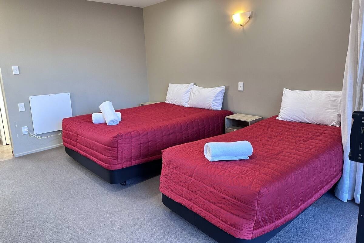 Ein Hotelzimmer mit zwei Betten, jeweils mit roter Bettwäsche und weißen Kissen, einem Nachttisch, einer Wandleuchte und einer Steckdose.