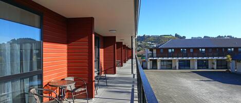 A balcony with a view of a building and a hilly landscape.