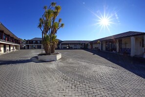 A courtyard with a paved floor, palm trees, and buildings with balconies and windows. - Heritage Court Lodge  (Oamaru)