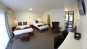 Ein Hotelzimmer mit zwei Betten, einem Schreibtisch, einem Sessel und einem Fernseher.