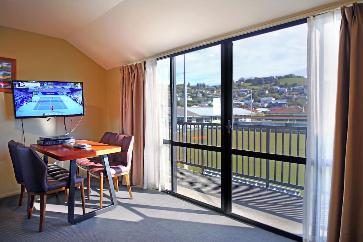 Ein Hotelzimmer mit großem Fenster, einem Tisch mit Stühlen, einem Fernseher und Blick auf eine Wohngegend.